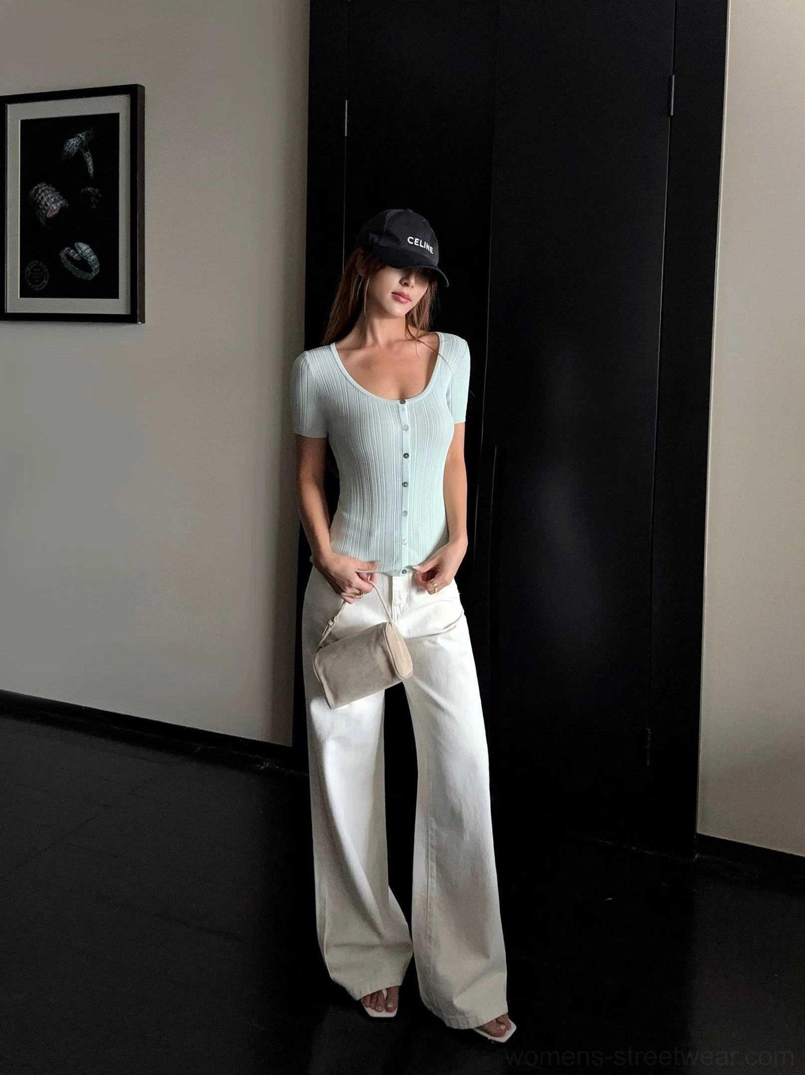 Full-body model wearing cream wide-leg denim streetwear pants with a mint ribbed knit top open-toe heels and a mini clutch in a dark studio