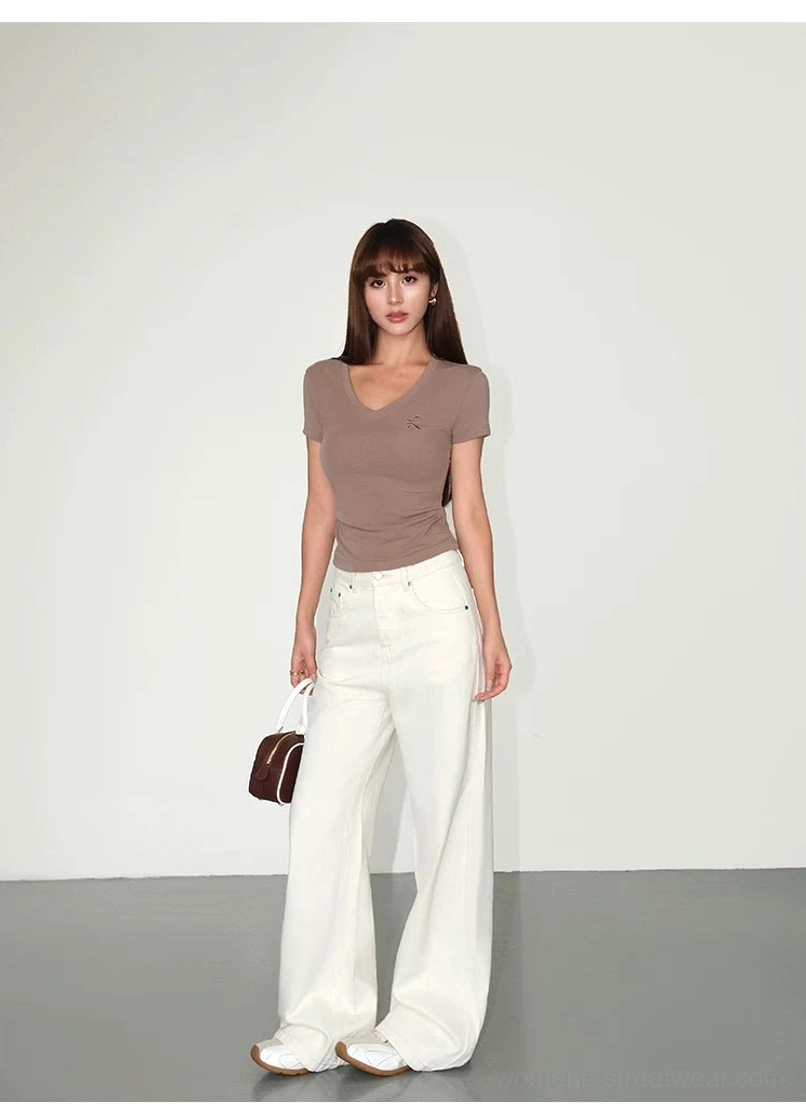 Full-body studio outfit featuring clean cream wide-leg denim streetwear pants with a taupe crew-neck top white flats and brown handbag