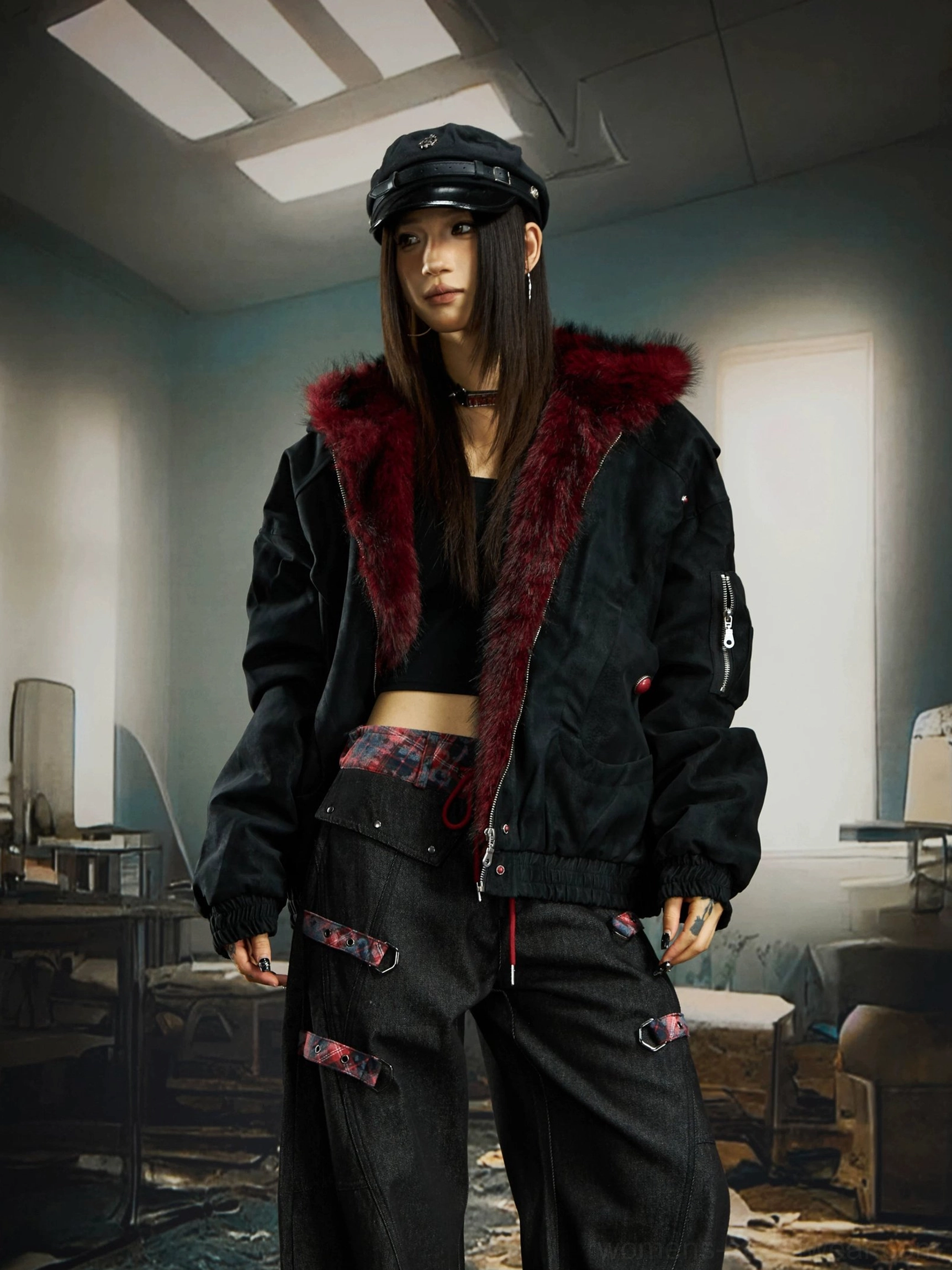 Female model wearing black oversized gothic bomber jacket with crimson faux fur hood trim and cargo pants in a retro office setting