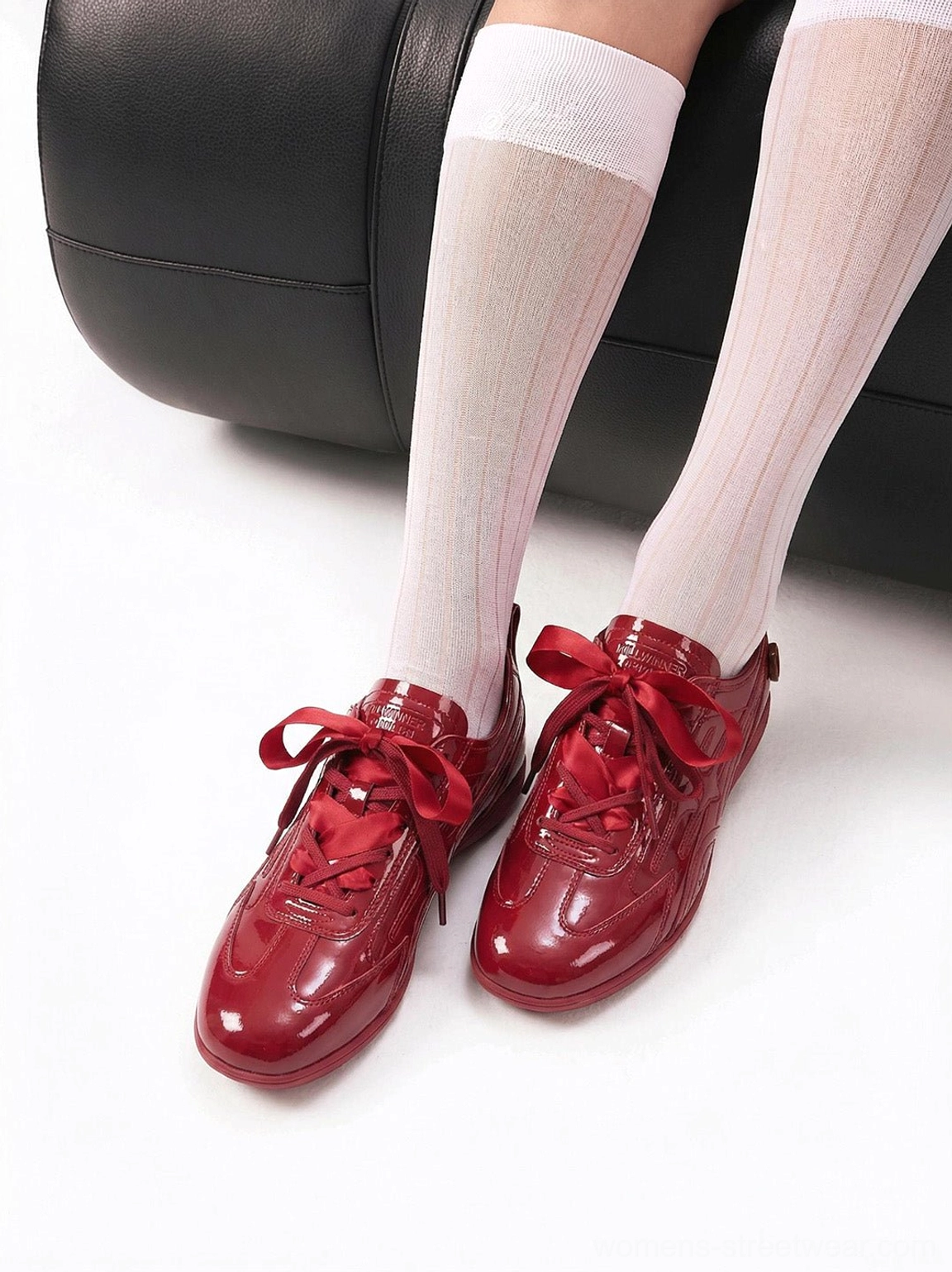 Side close-up of red glossy retro runner sneakers with satin-style bow laces and streamlined rounded toe