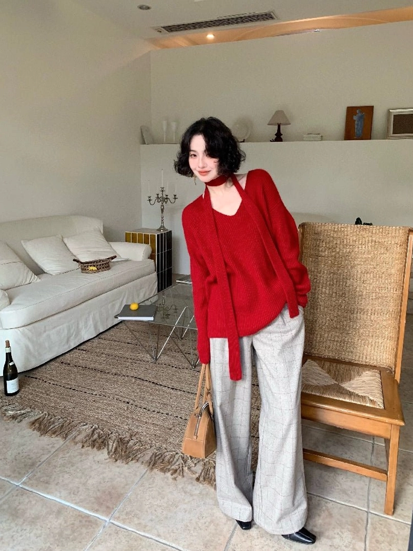 Crimson red ribbed V-neck scarf sweater worn with gray wide-leg trousers in a minimalist living room