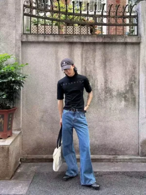 Side view of a black fitted mock neck graphic tee with subtle circular neckline studs styled with wide leg jeans and tote bag