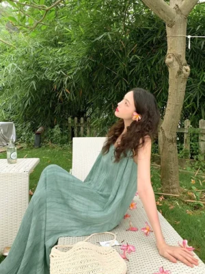 Sage green crinkled slip maxi dress with spaghetti straps and relaxed floor length silhouette styled in an outdoor garden