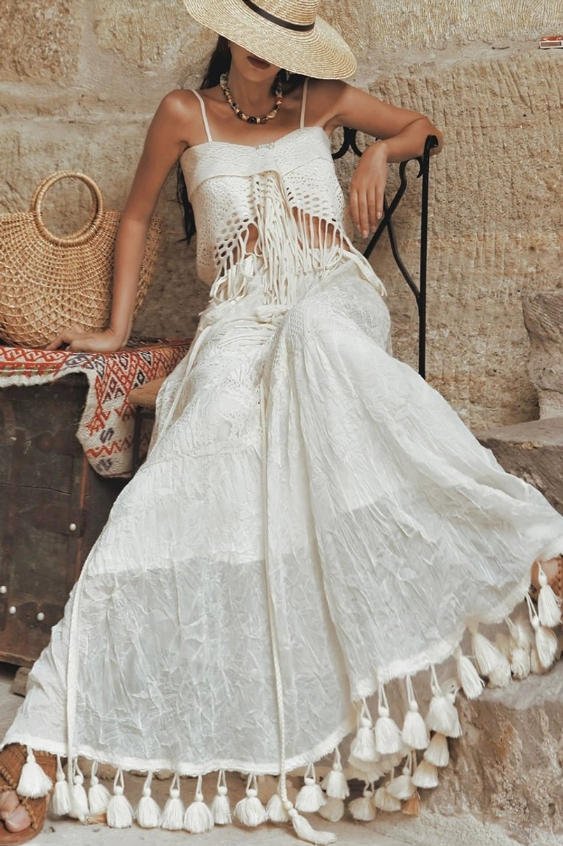 White crochet fringe maxi dress styling with delicate straps and tassel hem in a Mediterranean stone courtyard
