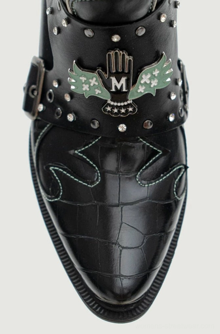 Close-up of a black crocodile-textured western boot toe with green contrast stitching, metallic studs, winged hand embroidery, and rhinestone accents