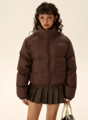 Dark brown cropped 90-fil puffer jacket with quilted texture and stand collar styled with pleated leather mini skirt