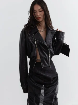Three-quarter view of a cropped black faux leather biker jacket for women with exposed silver zippers, oversized sleeves, asymmetrical closure, and modern Seoul streetwear styling