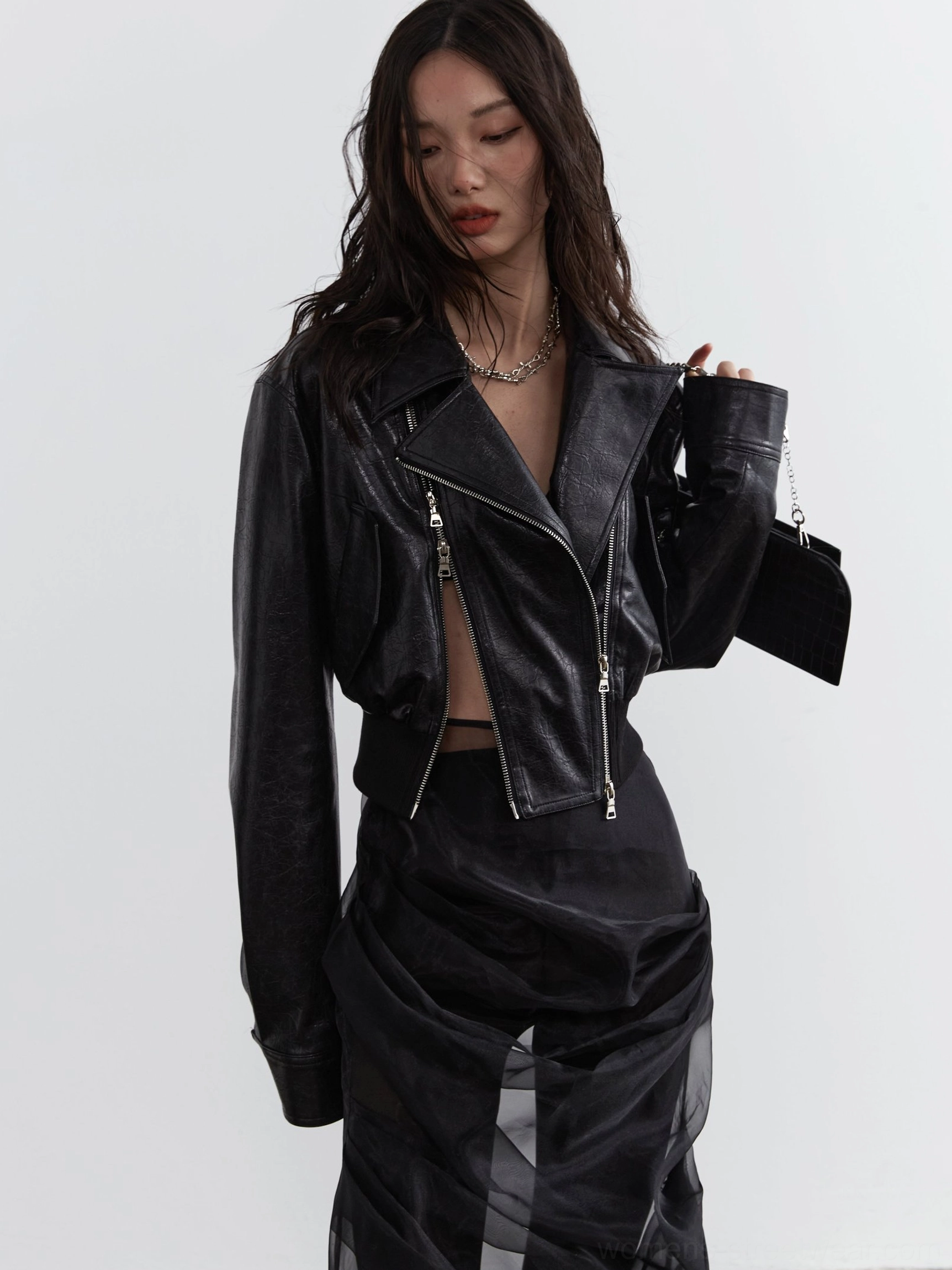 Three-quarter view of a cropped black faux leather biker jacket for women with exposed silver zippers, oversized sleeves, asymmetrical closure, and modern Seoul streetwear styling