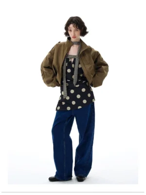 Female model wearing a cropped olive green utility bomber jacket with high stand collar, relaxed sleeves, and wide-leg denim in a white studio