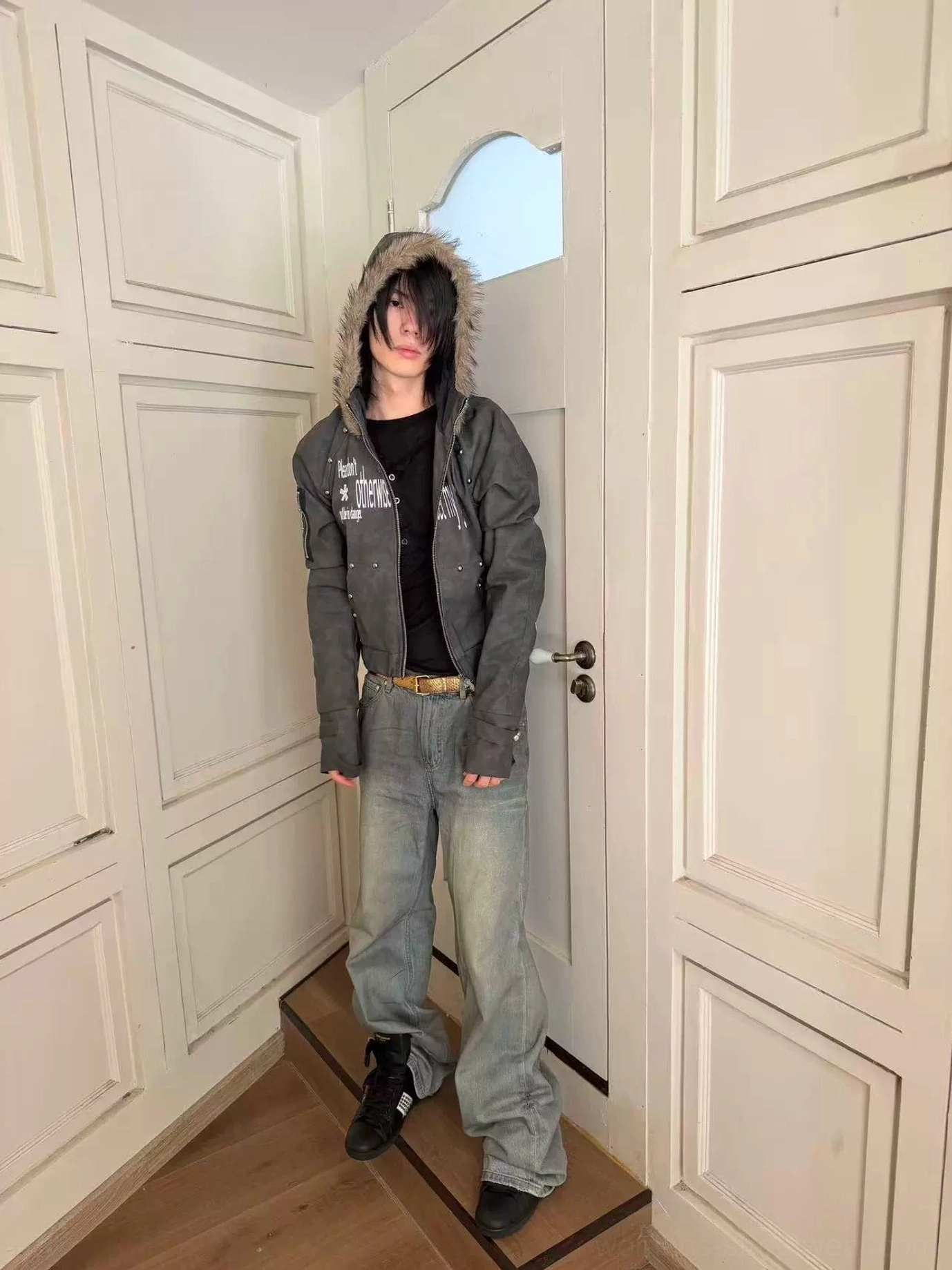Full body front view of a dark gray cropped PU hooded jacket with faux fur trim styled with loose light wash jeans