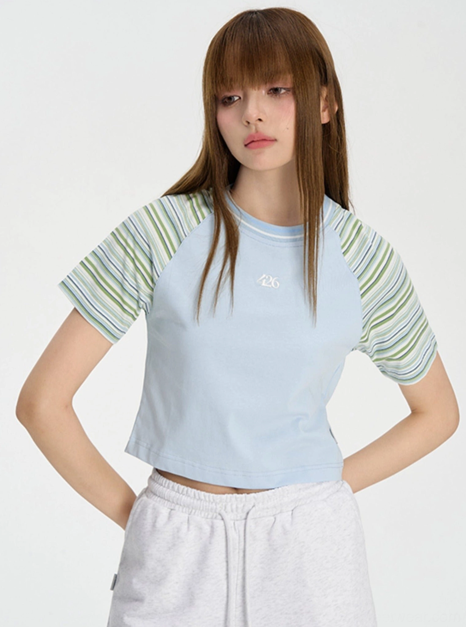 Blue cropped raglan baby tee with green pastel striped sleeves and small embroidered chest logo