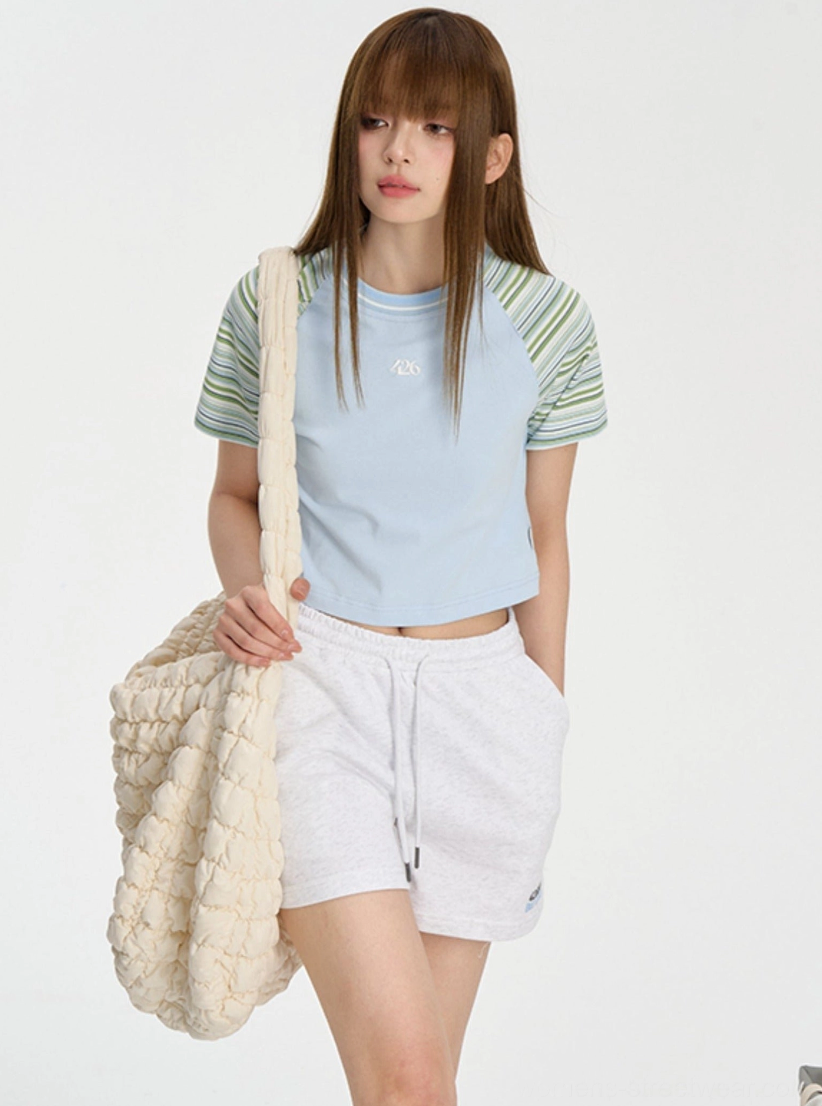 Blue cropped striped raglan tee paired with white sweat shorts and woven tote bag