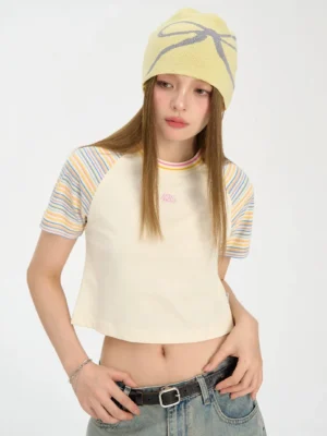 Close up of yellow cropped rainbow stripe raglan baby tee with pastel sleeves and embroidered chest detail