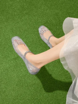 Woman wearing silver crystal glitter jelly Mary Jane flats with a sheer white midi skirt on green grass