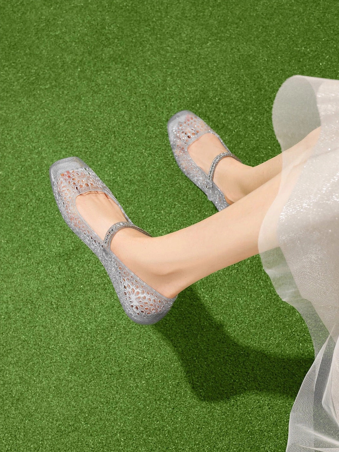 Woman wearing silver crystal glitter jelly Mary Jane flats with a sheer white midi skirt on green grass