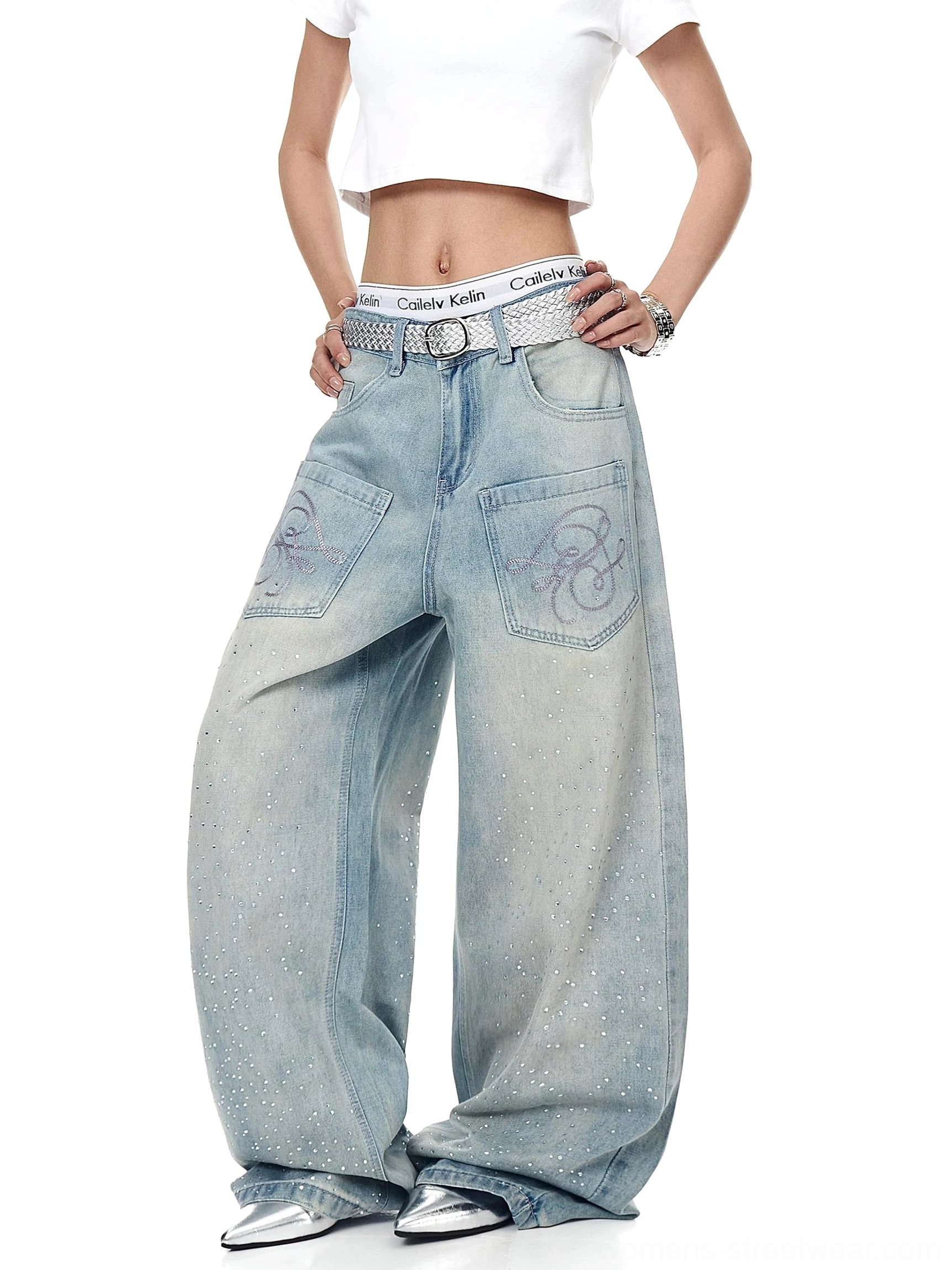 Front full-body view of ice-blue oversized wide-leg Y2K streetwear jeans with rhinestone starfall details, embroidered script patch pockets, silver belt, and cropped white tee