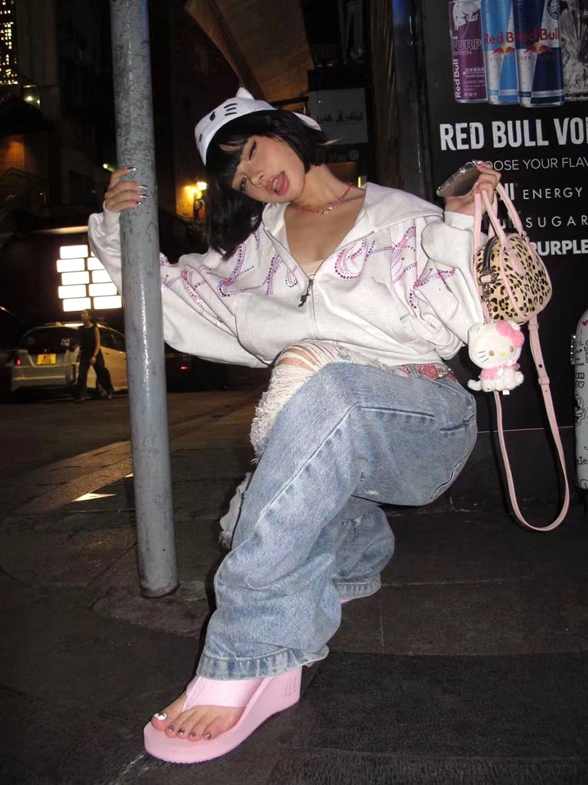 Pink wedge platform flip-flops worn with a white hoodie and baggy jeans in a nighttime streetwear setting