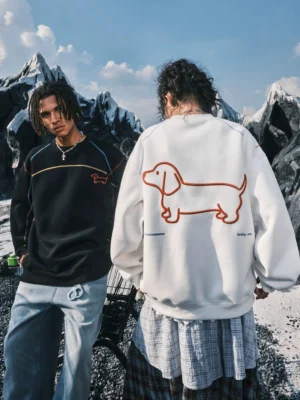 Two models wearing black and off-white dachshund embroidered oversized crewneck sweatshirts in a snowy mountain streetwear setting