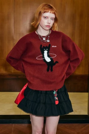 Dancing cat knitted sweater styled with black ruffled mini skirt and red waist bag in playful Korean street fashion outfit