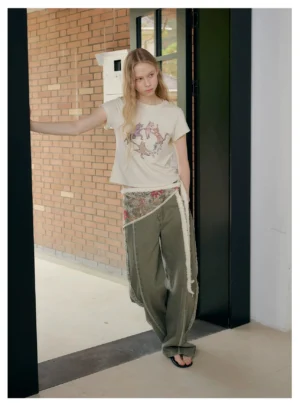 Front view of women wearing a playful dancing cat printed cropped T-shirt with army green wide-leg denim and a decorative waist scarf