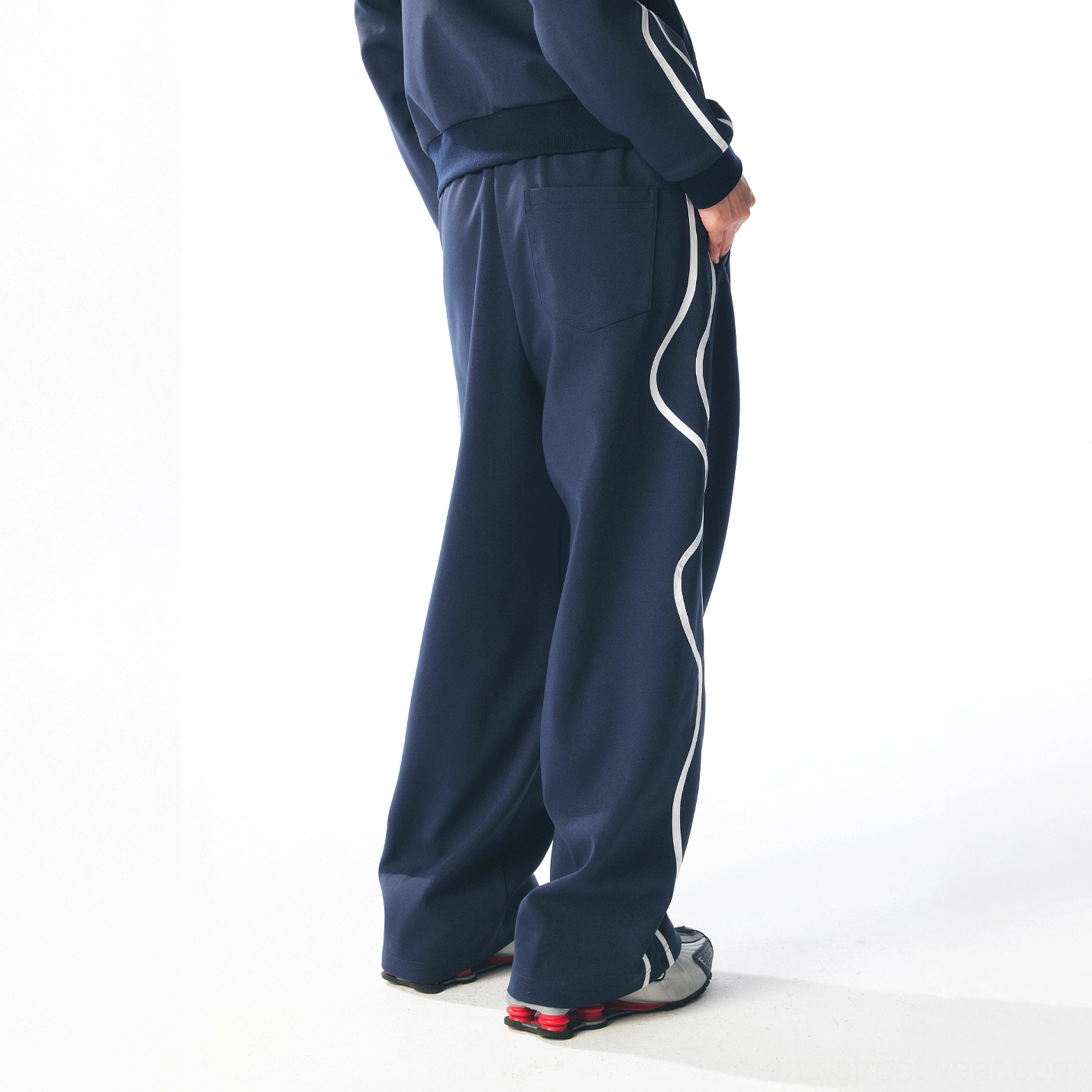 Back three-quarter view of dark blue curved stripe streetwear track pants with relaxed wide-leg fit