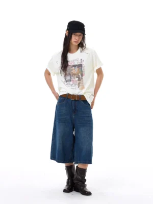 Front view of relaxed dark blue denim gaucho shorts with a cropped wide-leg silhouette styled with a black newsboy cap