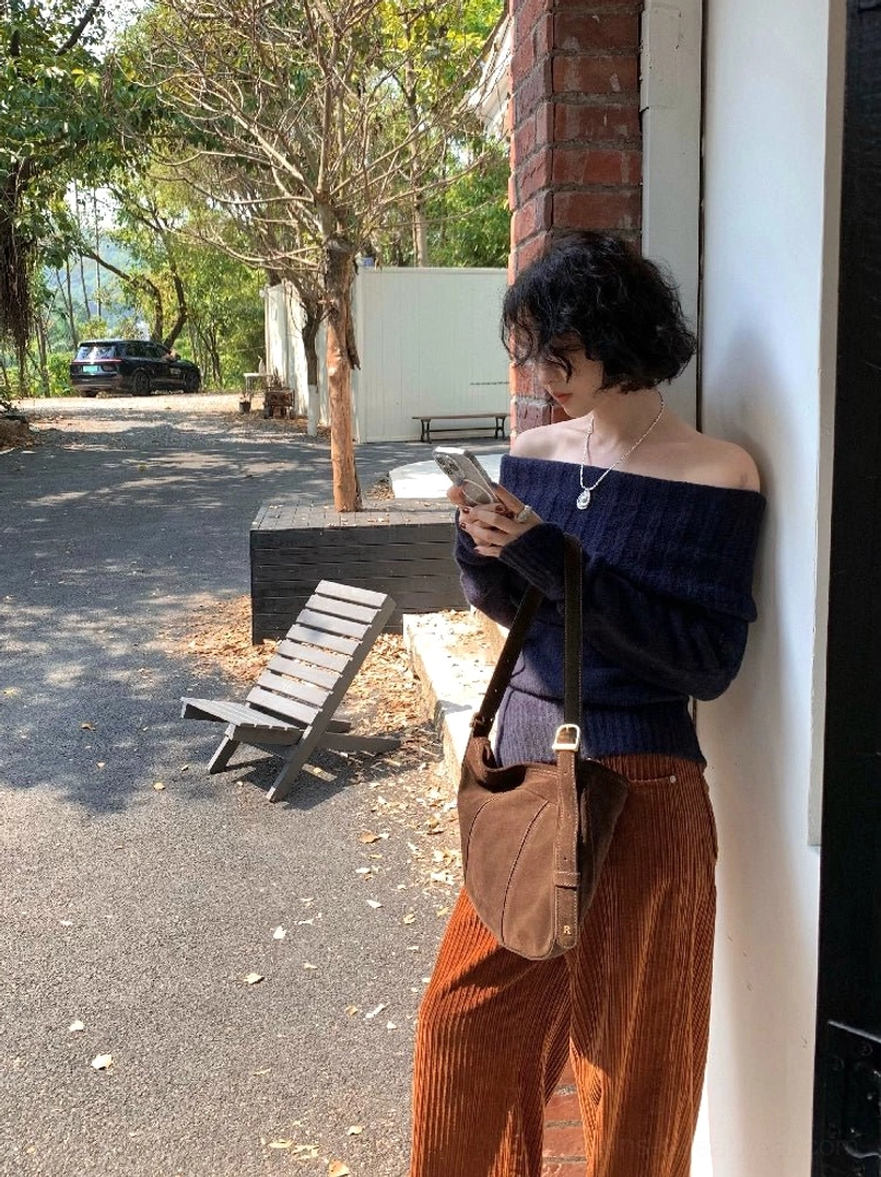 Dark blue women's off-shoulder knit sweater styled with caramel corduroy pants and a brown crossbody bag