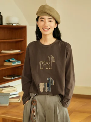 Dark brown abstract horse patch long sleeve T-shirt styled with grey wide leg pants and a beret in a vintage study setting