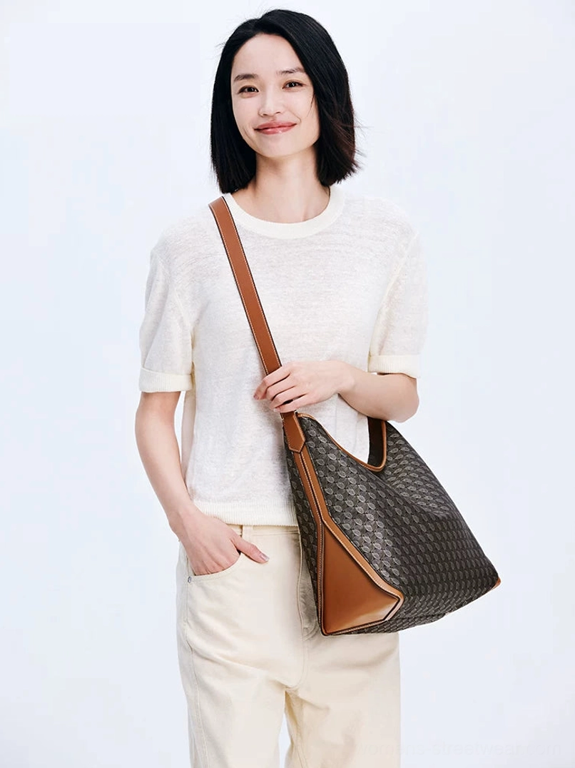 Model carrying dark brown monogram hobo shoulder bag with tan trim in casual neutral streetwear look