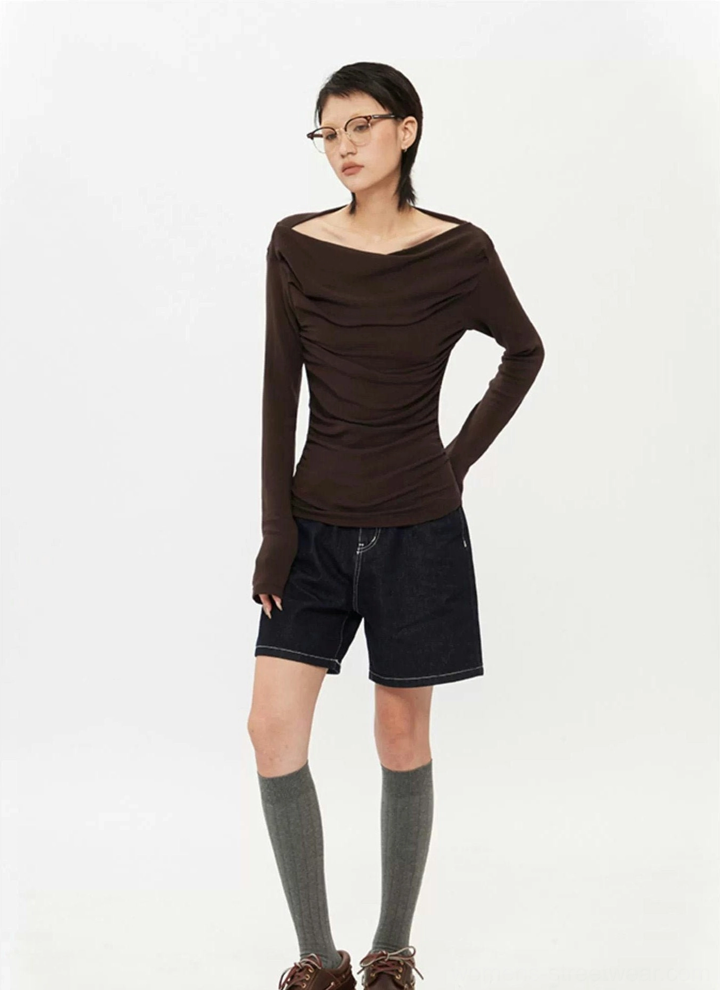 Full-body styling of dark brown off-shoulder ruched long-sleeve top with denim shorts, knee-high socks, and leather shoes