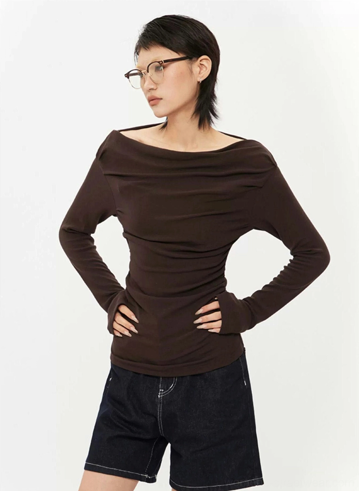 Three-quarter view of dark brown off-shoulder ruched top with folded neckline, slim long sleeves, and textured fitted streetwear design