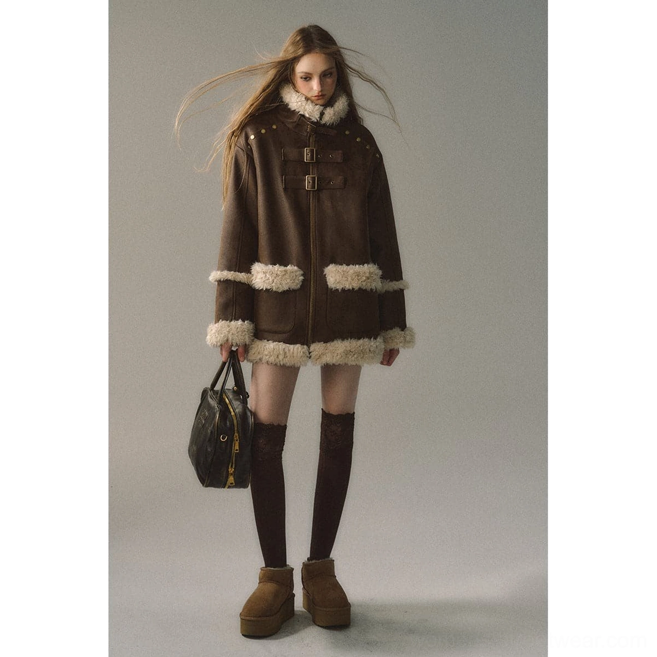Full-body fashion view of dark brown reversible suede shearling jacket with cream trims, platform boots, knee-high socks, and leather handbag