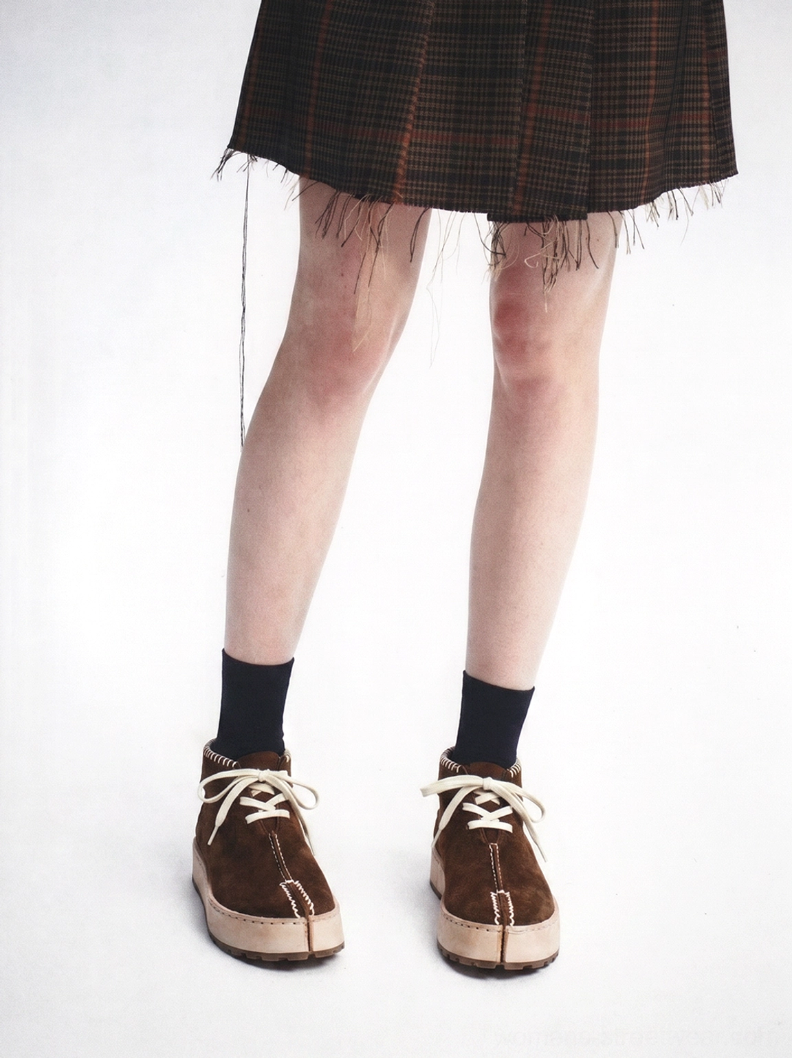 Dark brown split-toe lace-up chukka boots worn with a plaid fringe mini skirt and black crew socks