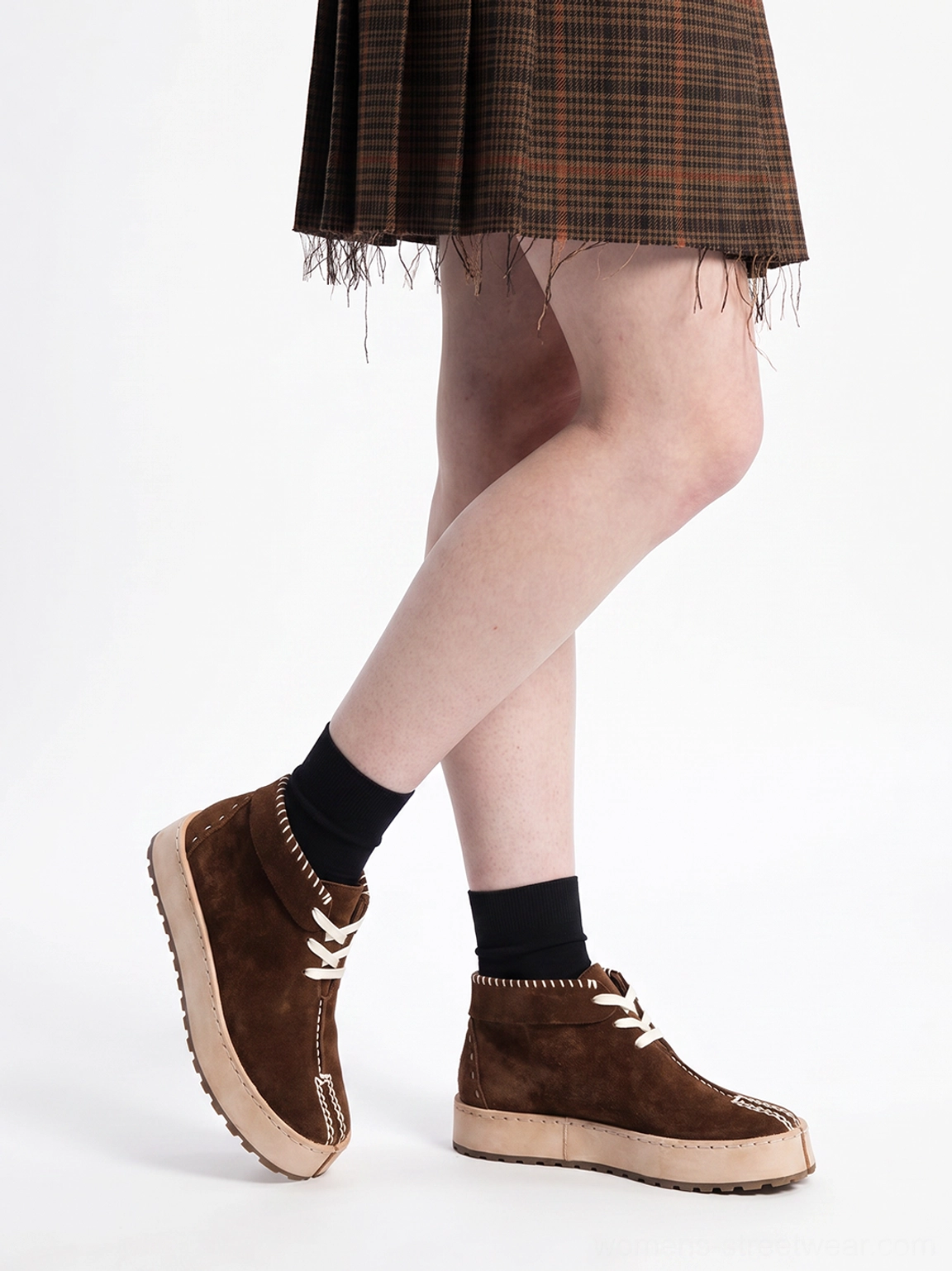 Side view of dark brown split-toe suede-finish chukka boots styled with a plaid skirt and black socks