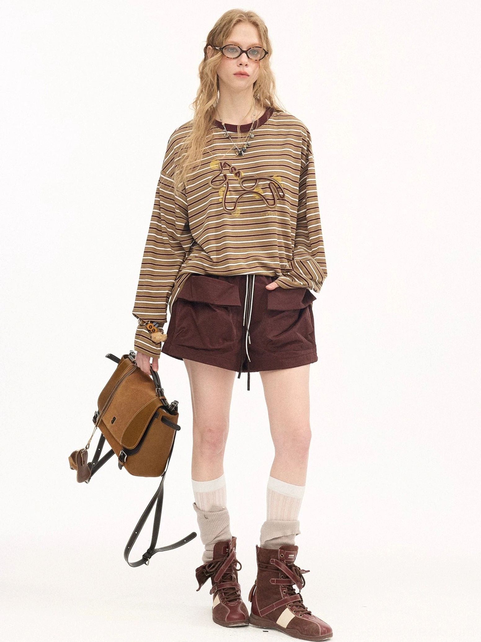 Dark brown streetwear cargo shorts with drawcord waist and oversized utility pockets styled with a striped graphic sweatshirt and crossbody bag