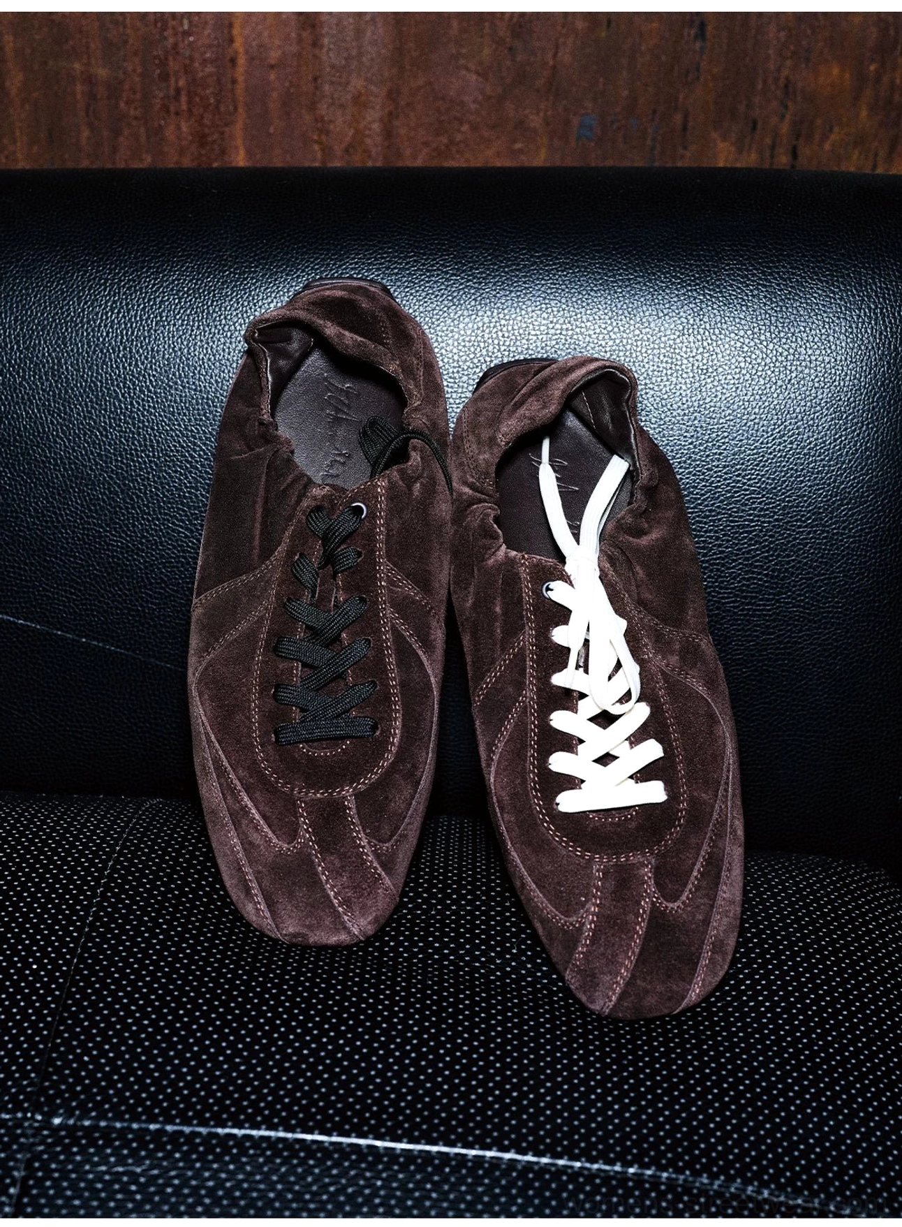Dark brown suede minimalist lace-up sneakers displayed with black and white flat lace options on a leather sofa
