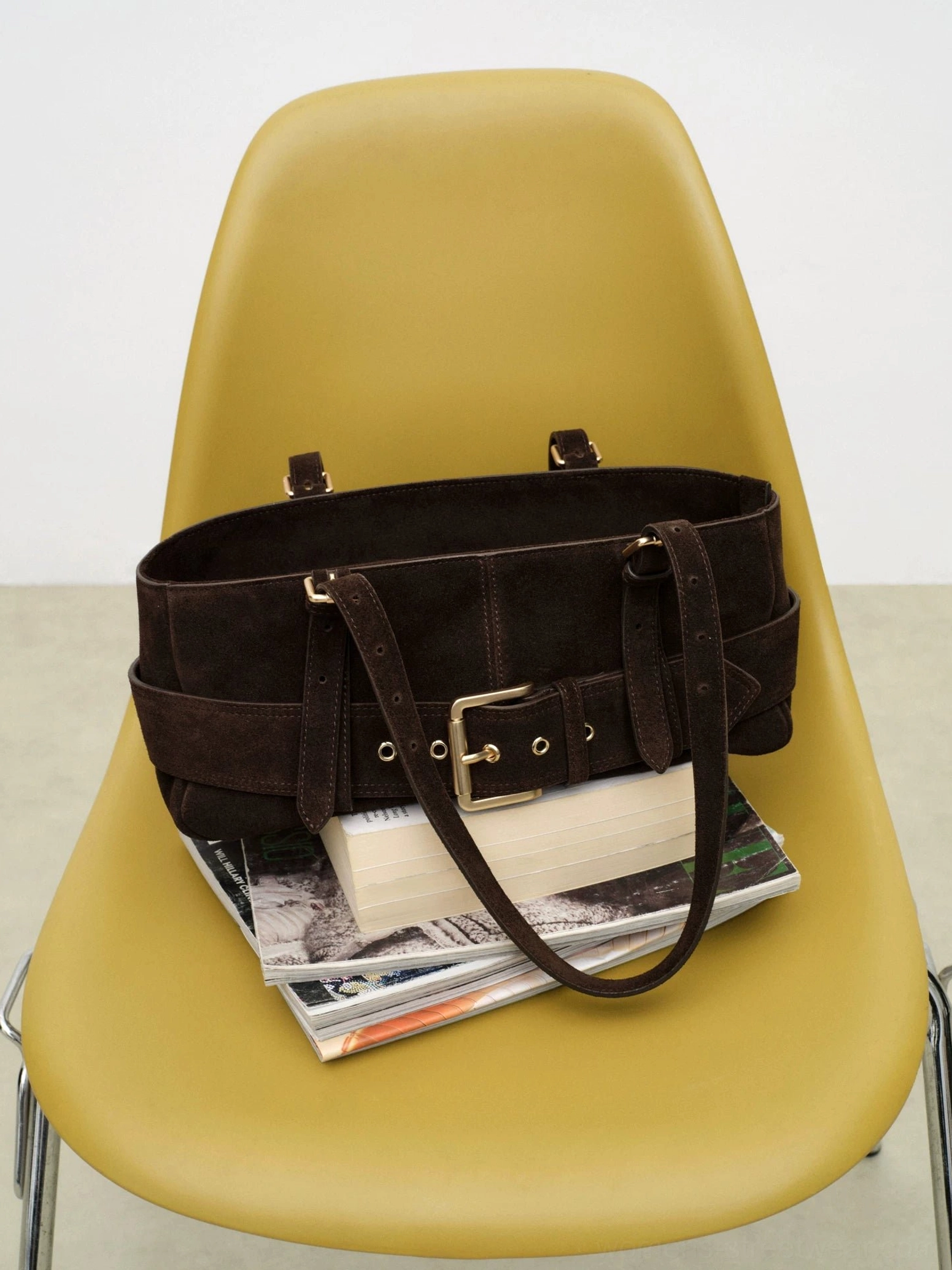 Dark brown weathered buckle baguette shoulder bag displayed on a yellow chair with adjustable shoulder straps and silver buckles