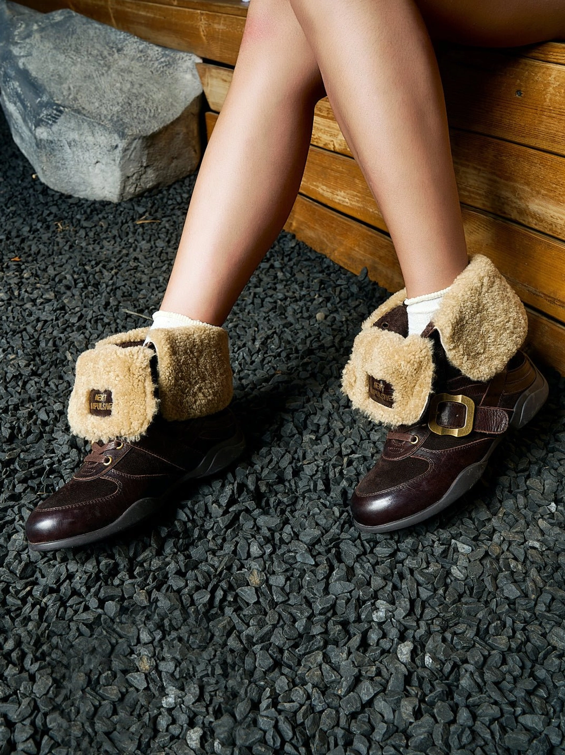 Side view of dark brown western shearling ankle boots worn with white socks showing the brass buckle