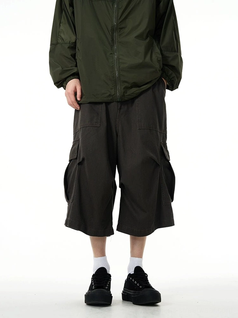 Dark charcoal wide-leg cargo pants with oversized side pockets styled with a dark green jacket and chunky black sneakers