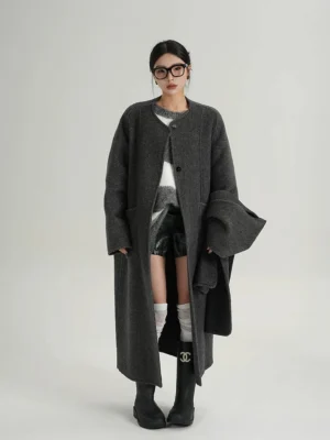 Front view of a dark charcoal wool cocoon coat with relaxed oversized fit, collarless neckline, button closure, and long dropped-shoulder streetwear silhouette