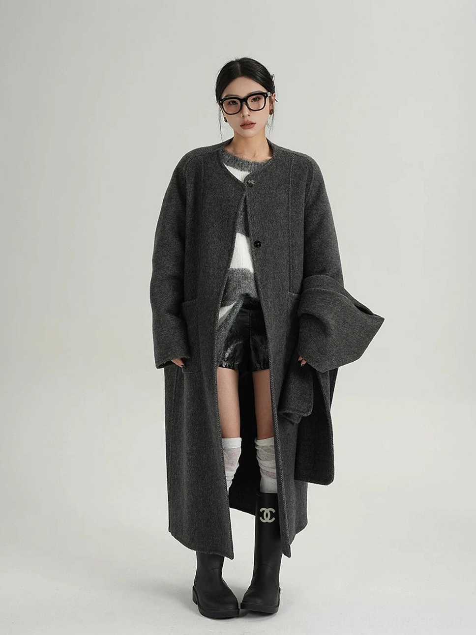 Front view of a dark charcoal wool cocoon coat with relaxed oversized fit, collarless neckline, button closure, and long dropped-shoulder streetwear silhouette