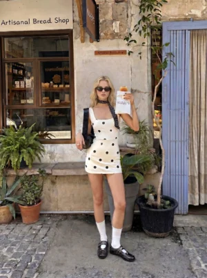 Woman wearing dark coffee square-toe buckle flats with a polka dot mini dress and white crew socks in a streetwear outfit