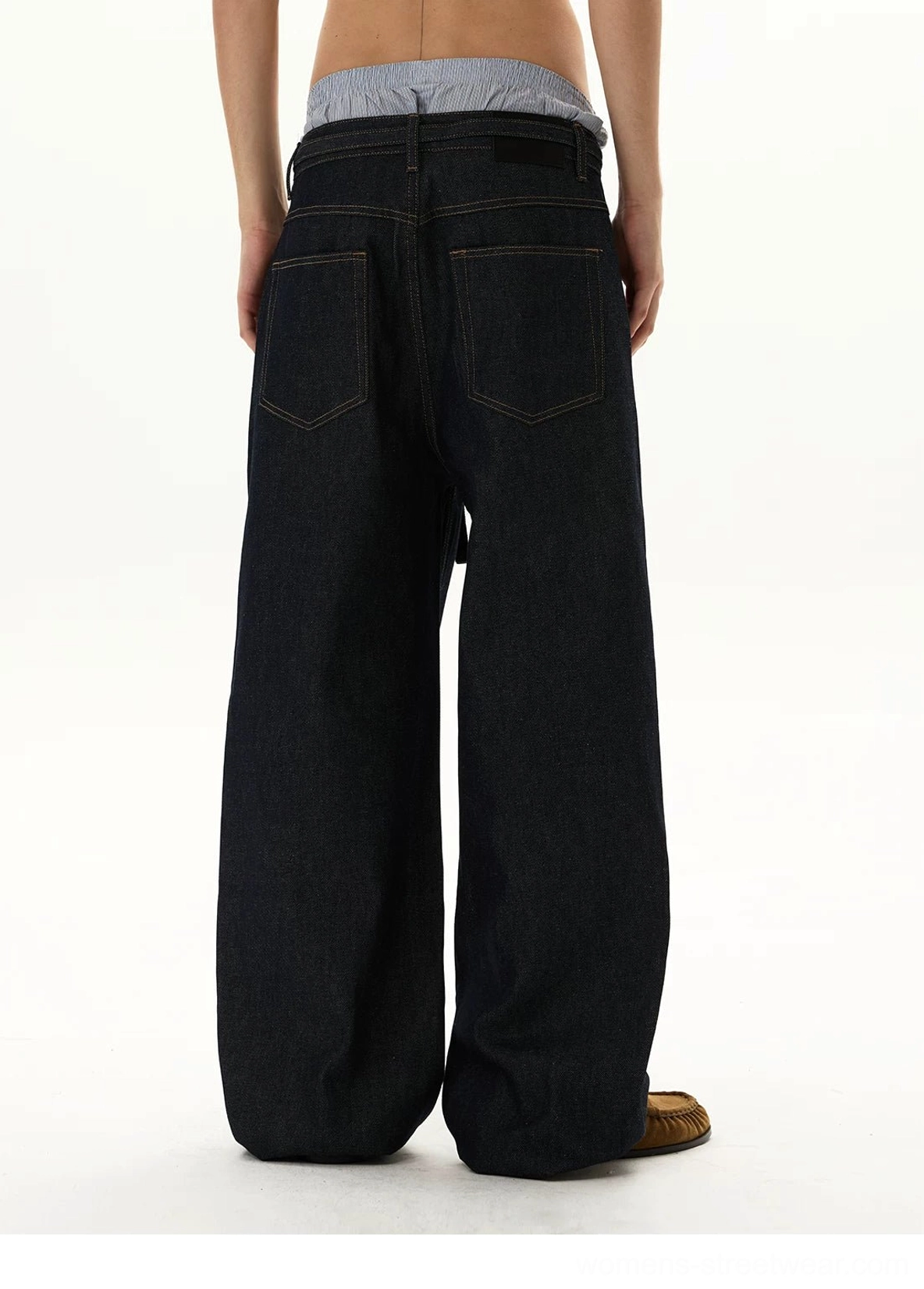Rear view of oversized dark denim balloon jeans on a model wearing a gray top, featuring back pocket stitching and stacked wide-leg hems