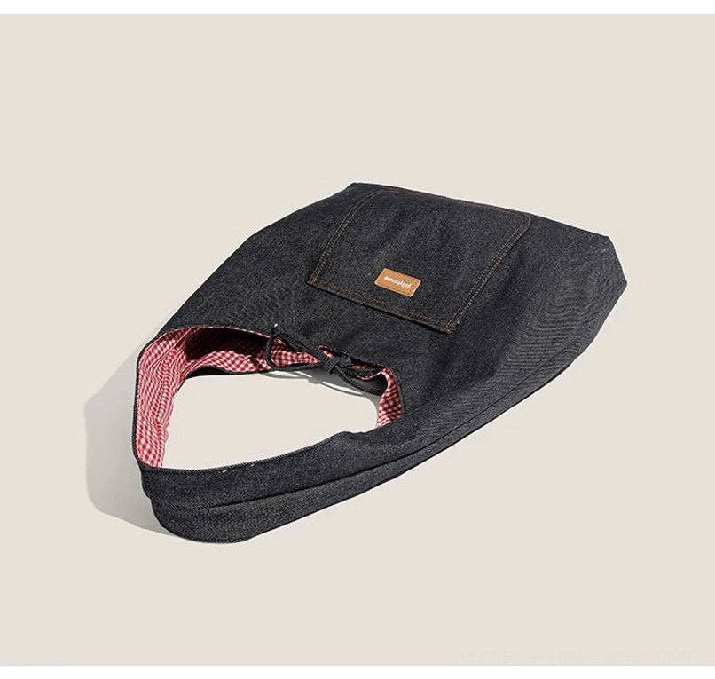 Folded dark denim drawstring shoulder tote with open red gingham lined interior on a neutral studio background
