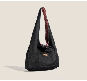 Dark denim drawstring sling tote bag with red gingham lining, front patch pocket, and slouchy hobo shoulder silhouette