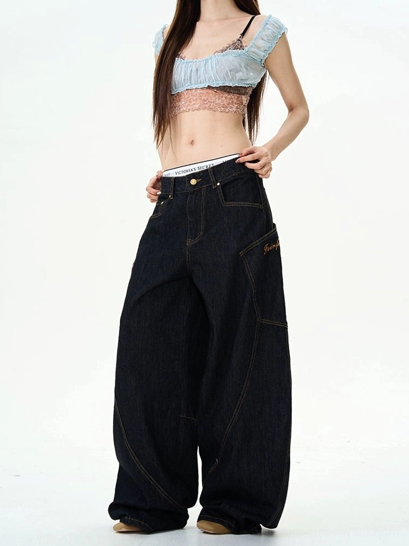 Front detail view of dark denim streetwear cargo pants showing button fly, metal rivets, curved seams, and wide-leg cut