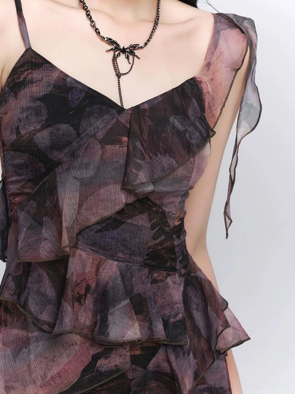 Close-up detail of a dark floral maxi dress with ruffled shoulder sash, layered front ruffles, sheer fabric, and romantic gothic styling