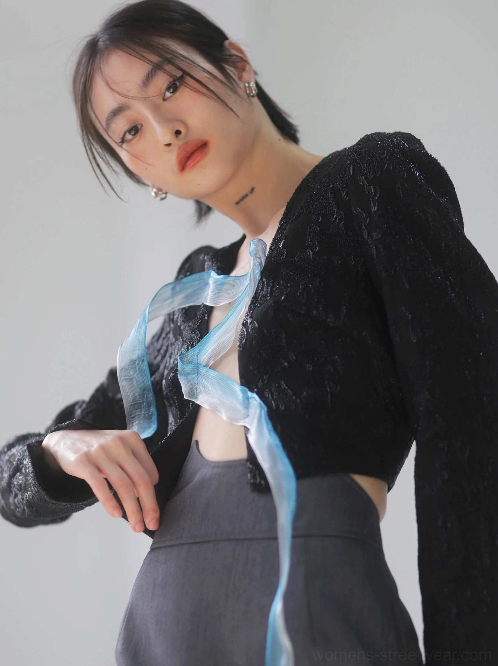 Close-up view of the dark gray asymmetric ruched skirt with tailored draping and stitched folds styled beneath a textured black cropped top and blue organza strap