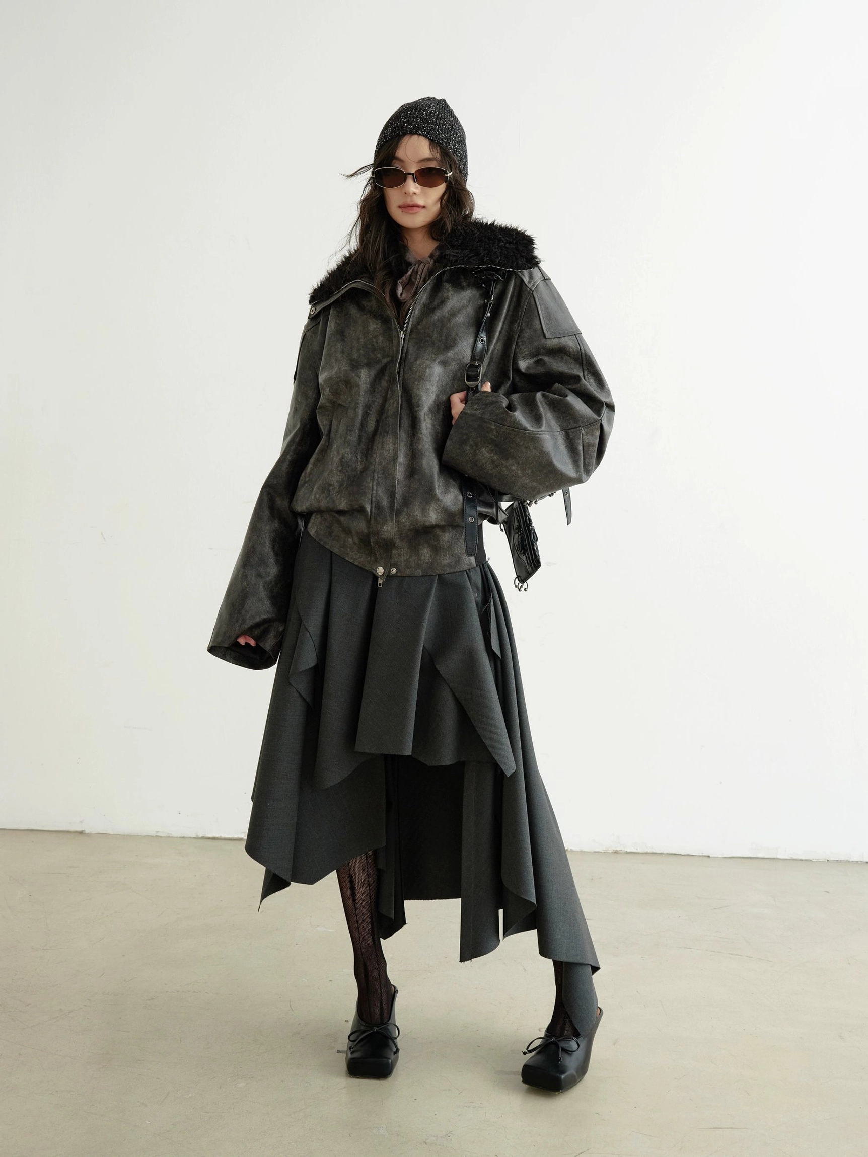 Dark gray asymmetrical layered midi skirt styled with a distressed leather bomber jacket in an avant-garde streetwear full body front view