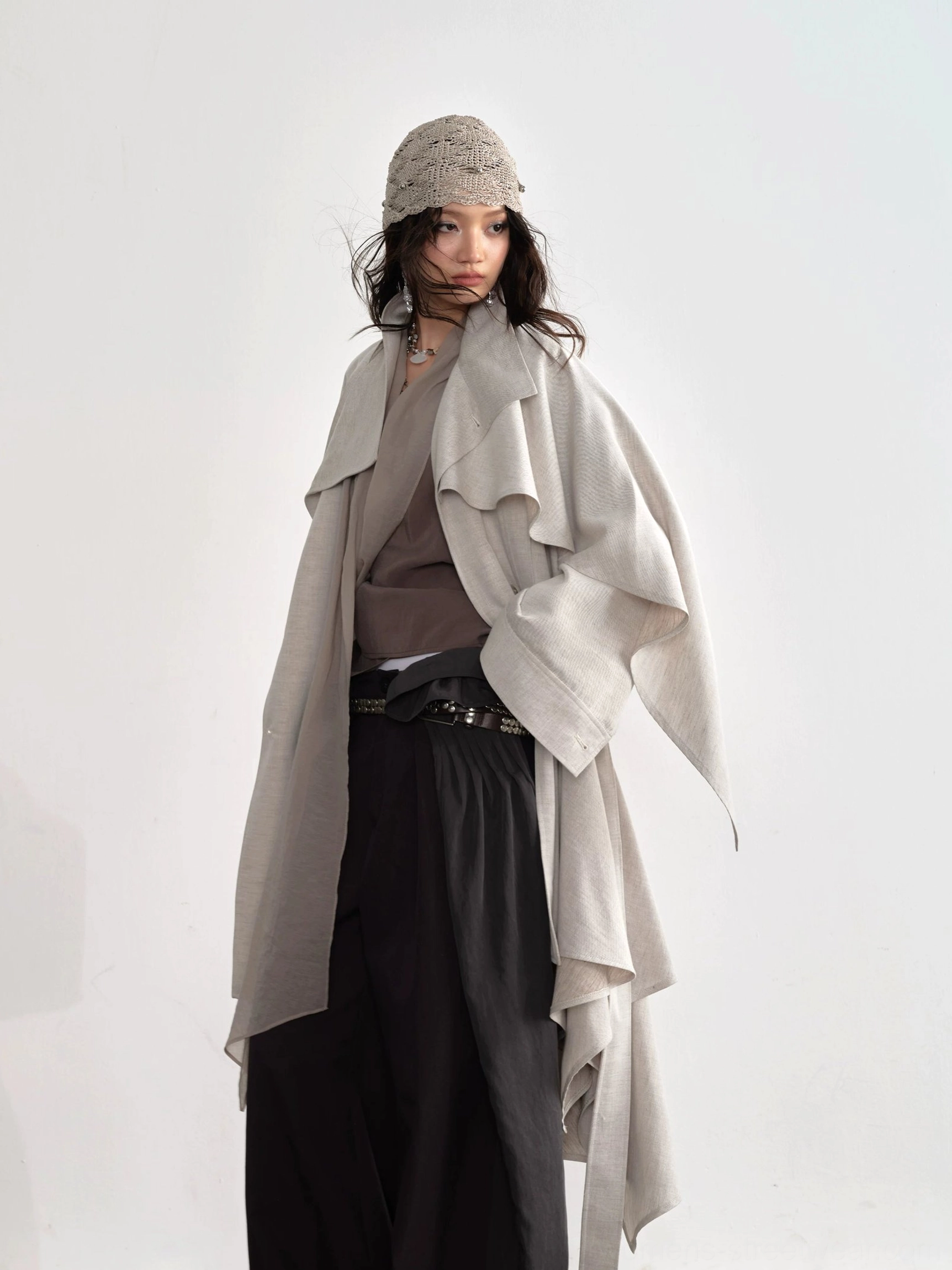 Dark gray deconstructed balloon pants with tie waist styled under oversized asymmetric trench coat